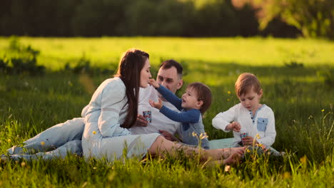 Father-mother-and-two-children-and-sitting-in-a-meadow-at-sunset-eating-ice-cream-in-the-summer-on-a-picnic.